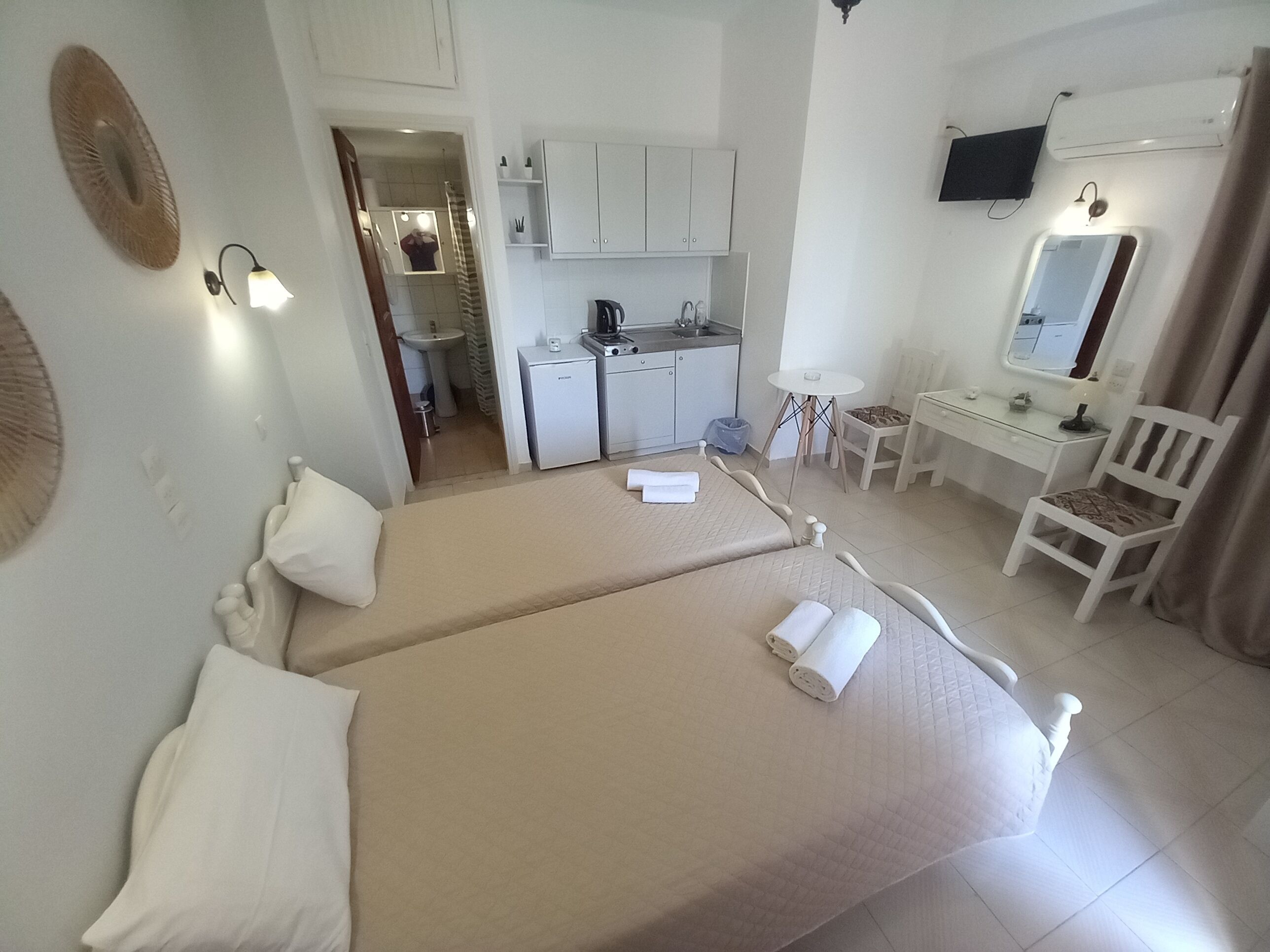A hotel room with two beds, a desk, a chair, a small kitchenette, and a bathroom.