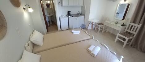 A hotel room with two beds, a desk, a chair, a small kitchenette, and a bathroom.