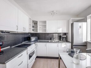 A modern kitchen with white cabinets, a black countertop, a microwave, a stove, and a refrigerator. - 4 Star Holiday Home in Lokken (Lokken)