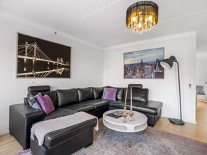 A modern living room with a black leather sofa, a round coffee table, and two paintings on the wall. - 4 Star Holiday Home in Lokken (Lokken)