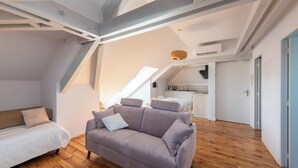 Avoin, loft-tyylinen huone, jossa on kalteva katto, sohva, sänky ja keittiöalue.