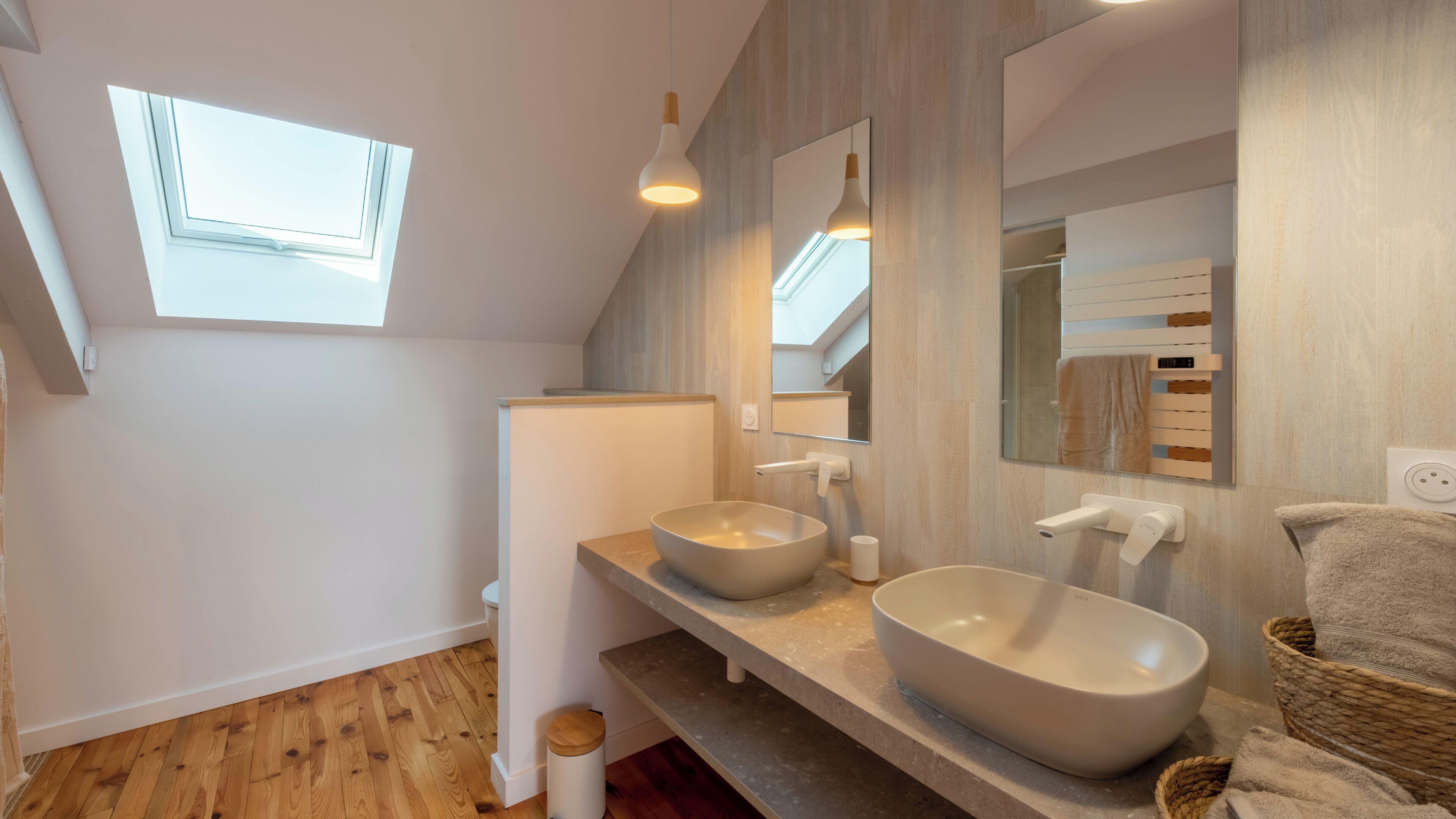 Une salle de bain moderne dotée d’un puits de lumière, de deux vasques, d’un miroir et d’un porte-serviettes.