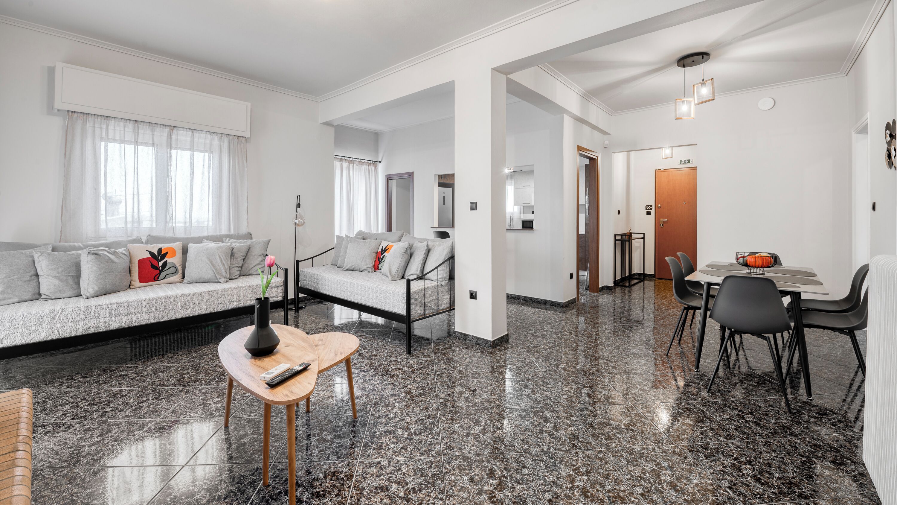 A modern living room with a sofa, a coffee table, and a dining area with chairs and a table.