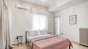 Een slaapkamer met een bed, airconditioning, raam met gordijnen, nachtkastje en radiator.
