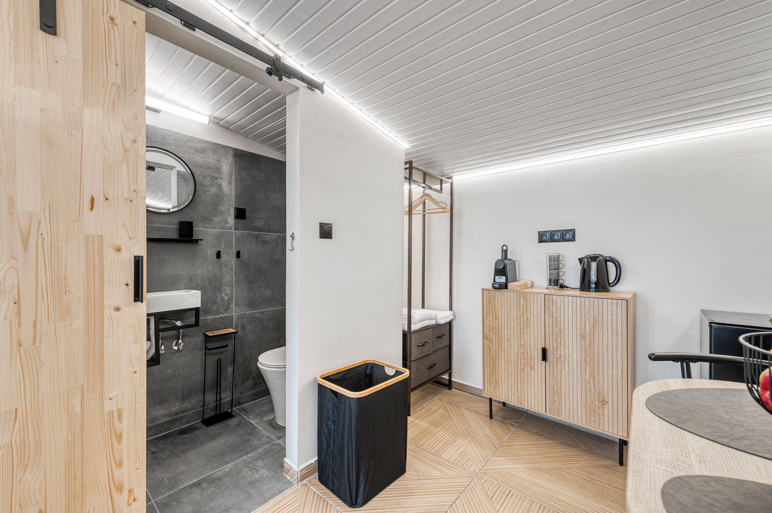 A modern bathroom with a wooden vanity, a sink, a mirror, a towel rack, and a cabinet with a kettle.