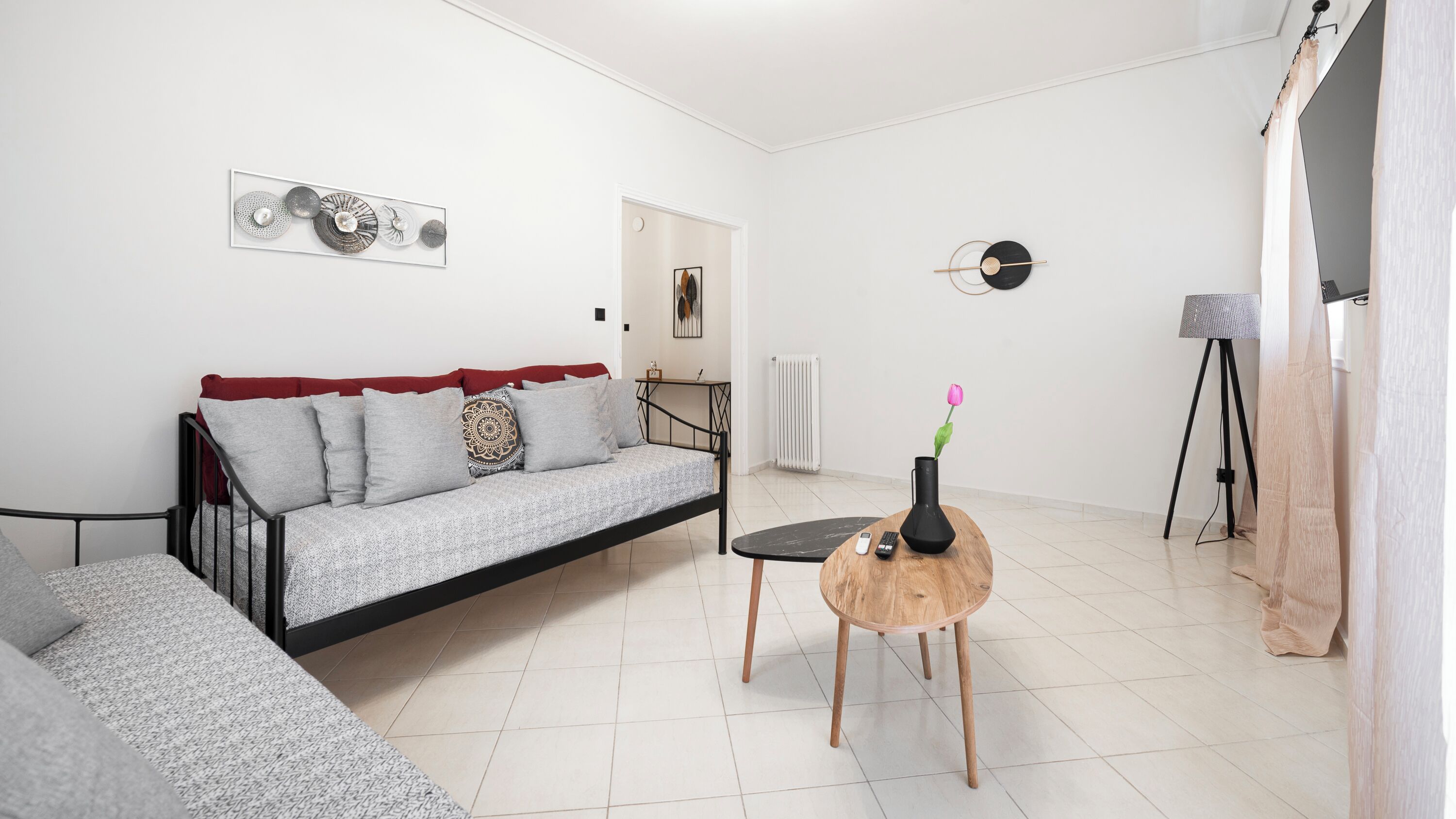 En moderne stue med en sofa, et lille rundt bord med en vase og en fjernbetjening, en gulvlampe og en radiator.