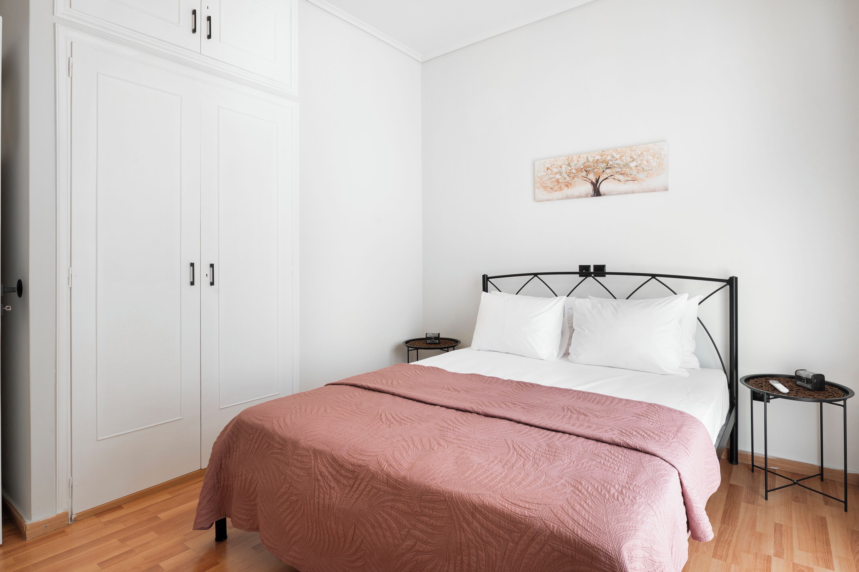 A bedroom with a bed, a bedside table, a nightstand, a wardrobe, and a wall-mounted artwork.