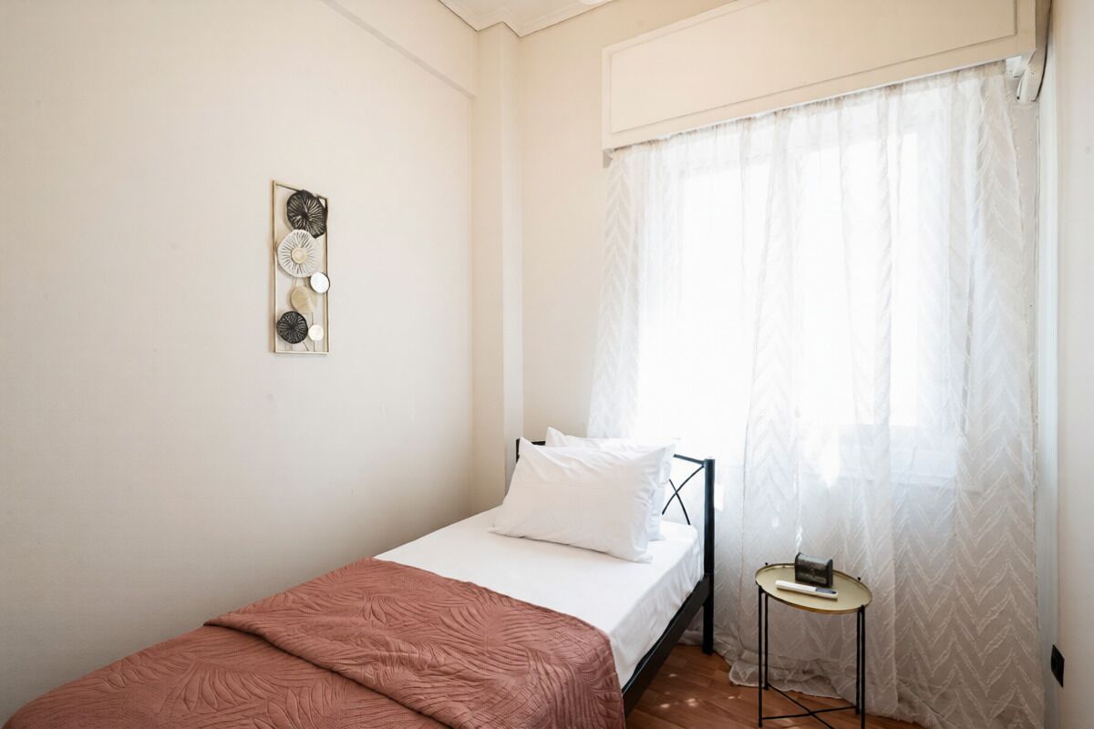 Una cama individual con colchón blanco y manta marrón, una mesita de noche con un libro y un objeto pequeño, y un adorno de pared.