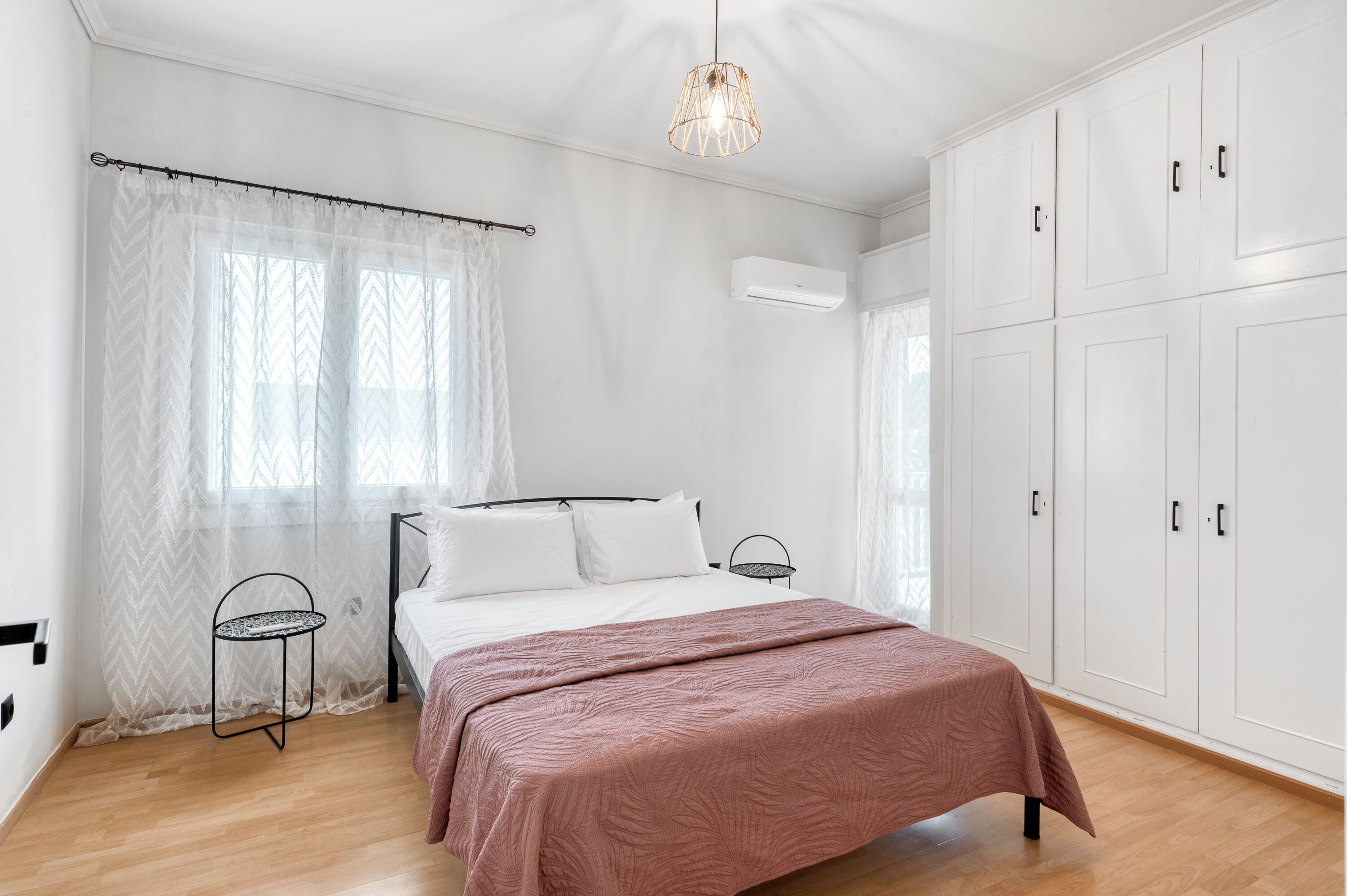A bedroom with a bed, a bedside table, a hanging light fixture, a wardrobe, and an air conditioning unit.
