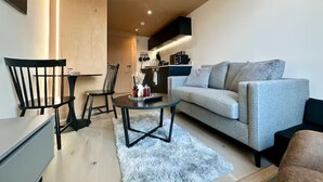 Ein modernes Wohnzimmer mit einer Couch, Sesseln, einem Couchtisch und einer Küchenzeile im Hintergrund.