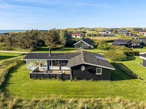 A modern house with a large glass balcony, surrounded by a well-maintained lawn and a view of a coastal area. - 4 Star Holiday Home in Lokken (Lokken)
