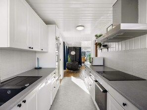 A modern kitchen with white cabinetry, a central island, and a view into the dining area. - 4 Star Holiday Home in Lokken (Lokken)