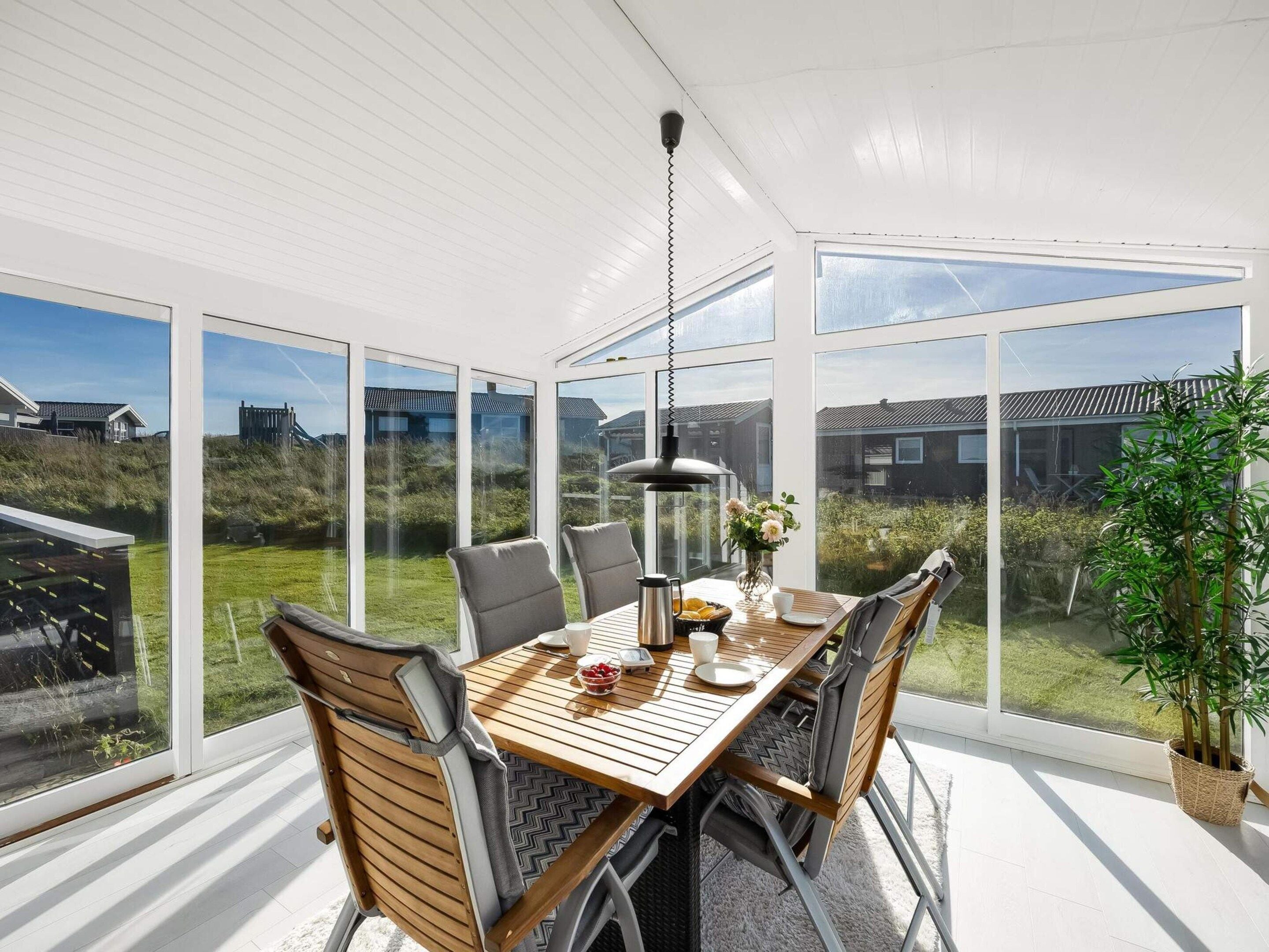 A conservatory with a dining table, chairs, and a hanging light fixture.