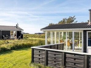 A modern house with a glass conservatory, a patio with outdoor furniture, and a well-maintained lawn. - 4 Star Holiday Home in Lokken (Lokken)