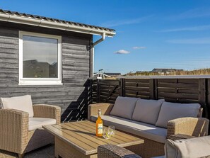 A wooden exterior wall with a window, wicker furniture, and a table with a bottle and glasses. - 4 Star Holiday Home in Lokken (Lokken)