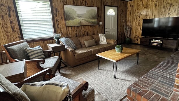 Een woonkamer met een bank, fauteuil, salontafel, televisie en een open haard.