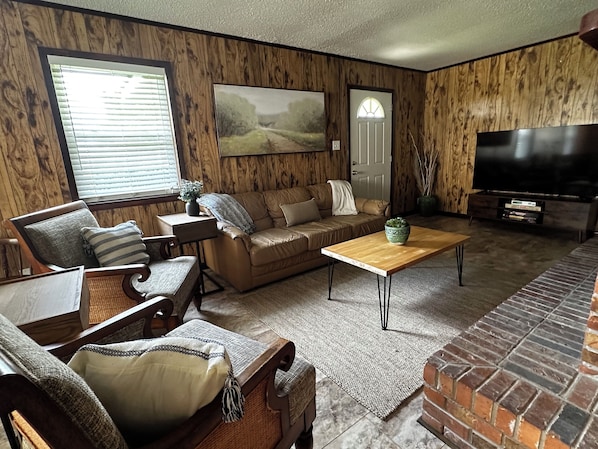 A living room with a sofa, armchair, coffee table, TV, and a fireplace. - Family-Friendly 4BR Getaway Close to Beaches, Fairhope & Fishing (Summerdale)
