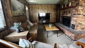 Een gezellige woonkamer met een leren bank, een houten salontafel, een televisie en een open haard van baksteen.