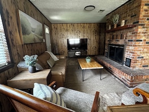 A cozy living room with a leather sofa, a wooden coffee table, a TV, and a brick fireplace. - Family-Friendly 4BR Getaway Close to Beaches, Fairhope & Fishing (Summerdale)