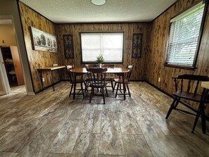 A dining area with a wooden table and chairs, a window with blinds, and a door leading to another room. - Family-Friendly 4BR Getaway Close to Beaches, Fairhope & Fishing (Summerdale)