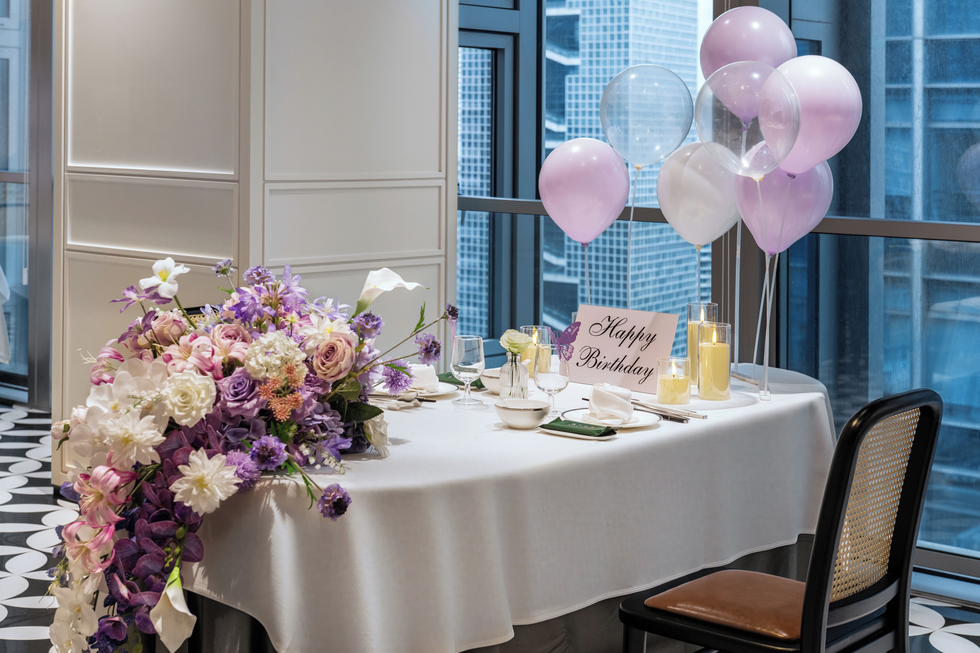 Una mesa dispuesta para una celebración de cumpleaños, con un centro de mesa floral, velas y un cartel que dice 'Happy Birthday'.