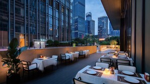 An outdoor dining area with tables set for two, surrounded by tall buildings. - IntercityHotel Shenzhen Bay (Shenzhen)