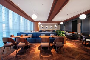 A modern restaurant with wooden flooring, blue seating, and pendant lighting.