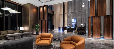 A modern lobby with seating, a reception desk, and a large digital display.