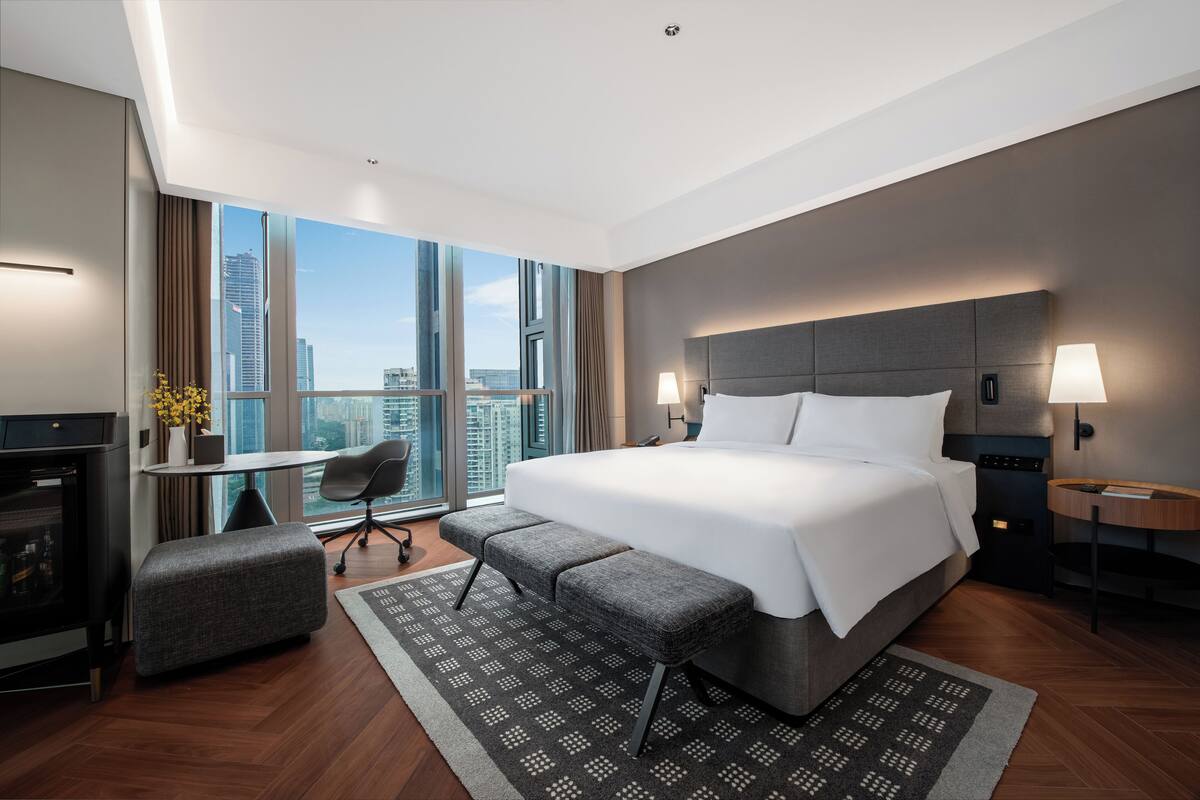 Ein modernes Hotelzimmer mit einem großen Bett, einem Schreibtisch und Blick auf die Stadt.