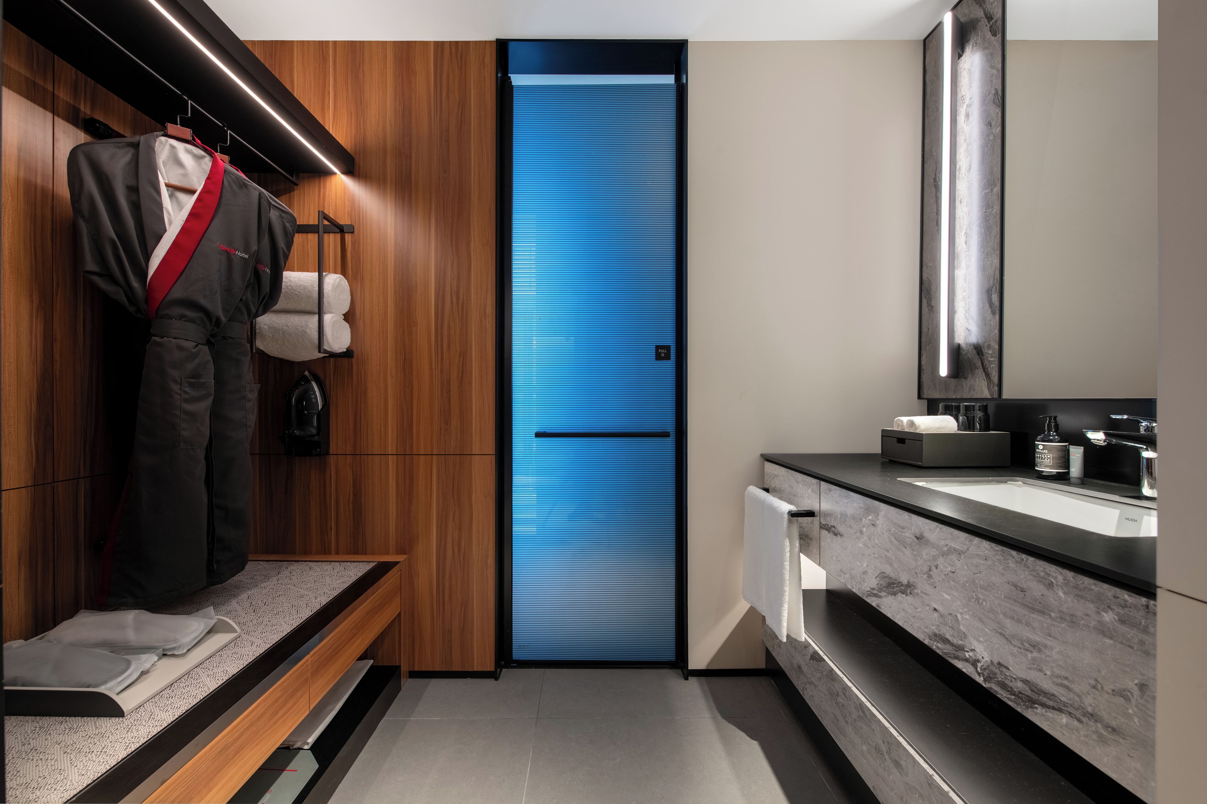 Ein modernes Badezimmer mit einem Holzboden, einer blauen Tür und einem aufgehängten Bademantel.