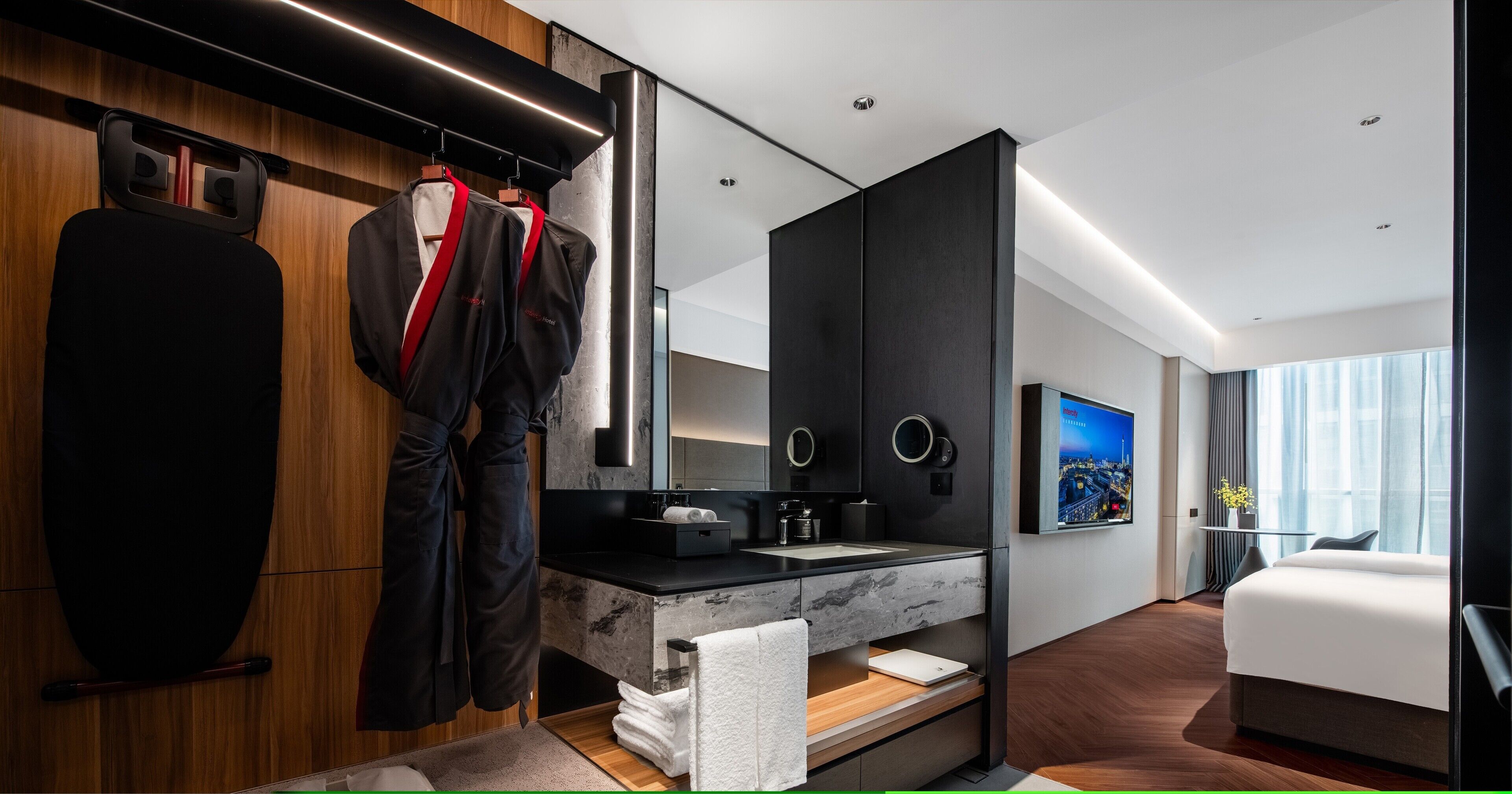 Ein modernes Hotelzimmer mit einem Holzschrank, einem großen Spiegel, einem Flachbildfernseher, einem Bett und einem Badezimmer mit Marmorplatte.
