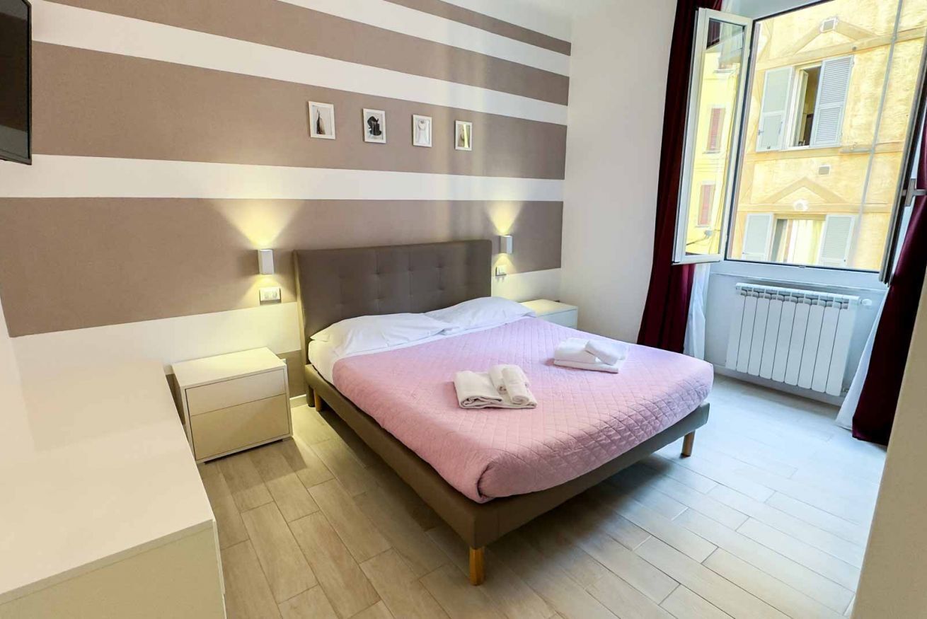 A bedroom with a bed, bedside tables, wall-mounted lights, a window with curtains, and a radiator.