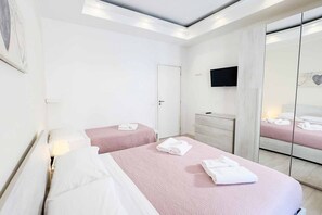 Hotellihuone, jossa on kaksi sänkyä, televisio, vaatekaappi ja peili.