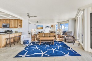 A spacious living area with a large blue rug, a leather sofa, a coffee table, and a kitchen area with wooden cabinets and a microwave. - Sea Gull #610L: Beachfront 2 Bedroom 2 Bathroom With Spectacular Views and 24 Hour Management (Port Aransas)