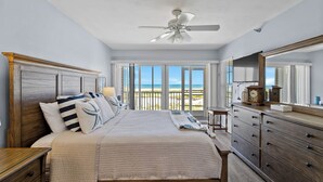 A bedroom with a bed, dresser, ceiling fan, and a balcony with a view.