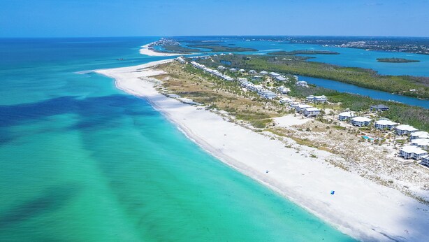 An aerial view of a coastal resort with a long beachfront, clear turquoise waters, and scattered buildings.