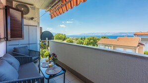 Un balcón con sofá, mesa y ventilador, con vistas panorámicas al mar y a las montañas.