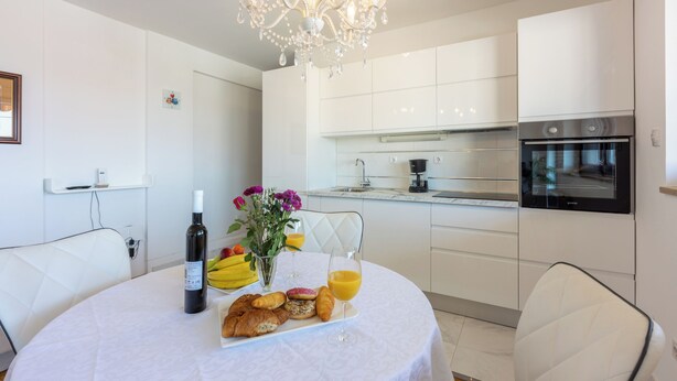 Una cocina moderna con armarios blancos, horno empotrado y zona de comedor con mesa lista para el desayuno.