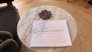 A round marble table with a document titled 'OUR WHITSUNDAYS' and a woven decorative item. - Escape to an adults only, coastal intimate retreat. (Hideaway Bay)