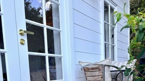 A house with a white exterior, a sliding glass door, a metal chair with cushions, and a welcome mat. - Escape to an adults only, coastal intimate retreat. (Hideaway Bay)