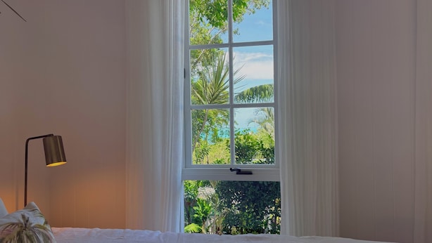 A bedroom with a large window, a bed, and a lamp. - Escape to an adults only, coastal intimate retreat. (Hideaway Bay)