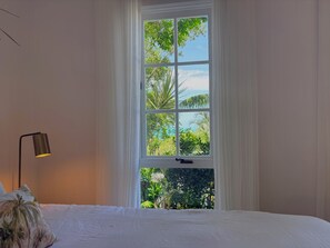 A bedroom with a large window, a bed, and a lamp.
