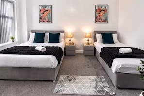 A hotel room with two beds, each with a pillow, a bedside table with a lamp, and a framed picture on the wall. - 30% off Comfortable 4-Bed Home 8 Beds Pets Welcome Sleeps 9 (Leeds)
