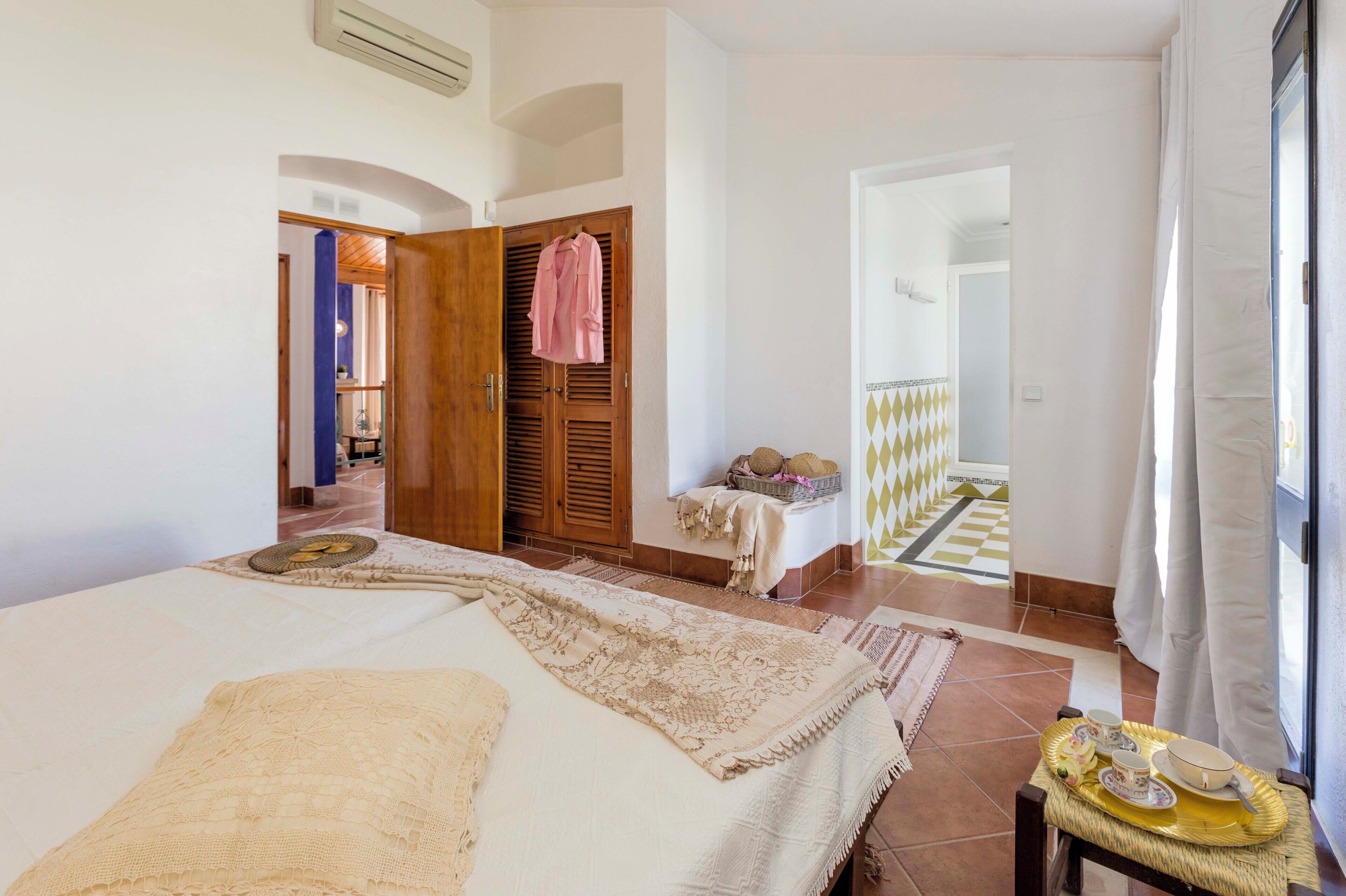 A hotel room with a bed, a small table with a tray, a wardrobe, and a view of the outside.