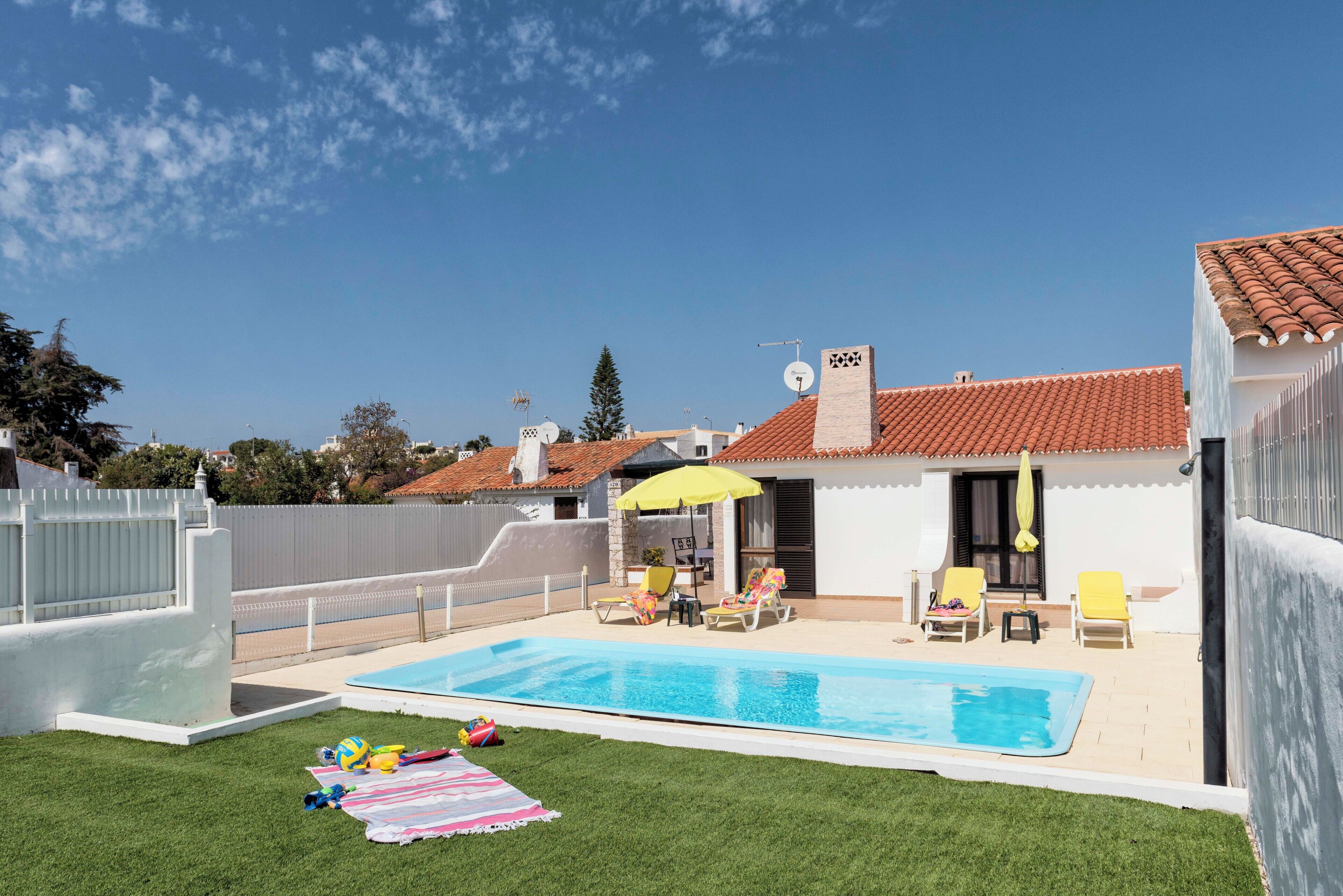 A backyard with a swimming pool, a white fence, and a house with a red-tiled roof.