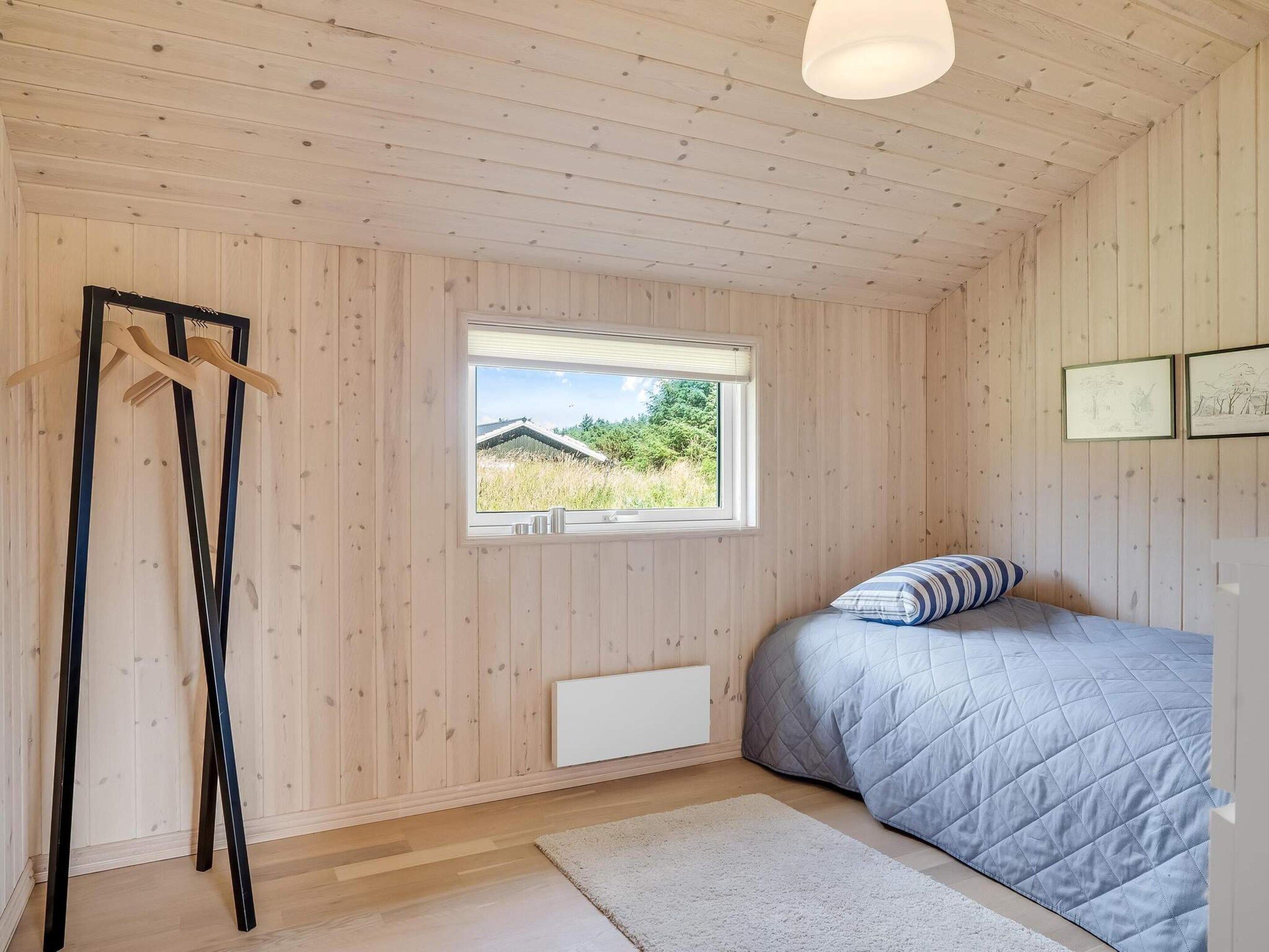 Ein Schlafzimmer mit einem Bett, einem Fenster, einer Heizung, einem Kleiderhaken und einer Deckenleuchte.