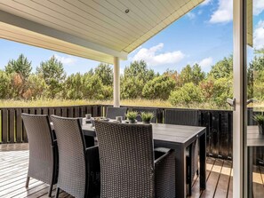 Eine Terrasse im Freien mit Tisch und Stühlen, umgeben von einer Holzterrasse und einem Glasgeländer.