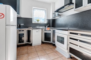 Une cuisine de taille réduite, dotée d’appareils électroménagers blancs, d’une fenêtre avec des rideaux et d’un sol carrelé.
