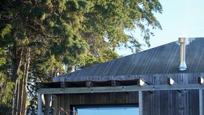 A rustic wooden building with a covered porch, steps leading to a door, and a view of the sea. - Quinta da Boa Esperança (Torres Vedras)