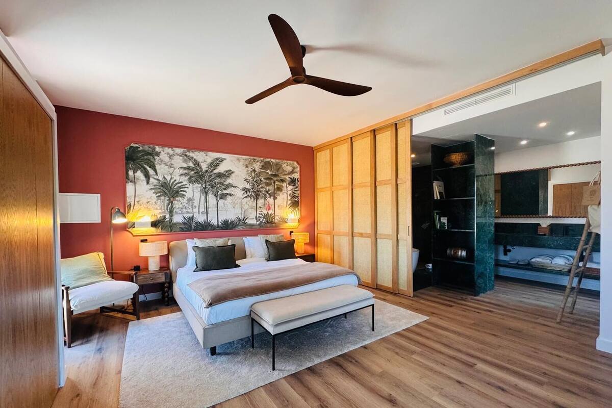 Une chambre à coucher avec un lit, des lampes de chevet, un ventilateur de plafond, un grand tableau et une armoire.